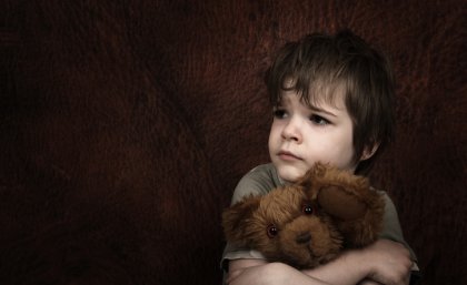 Young child looking distressed and holding teddy bear.